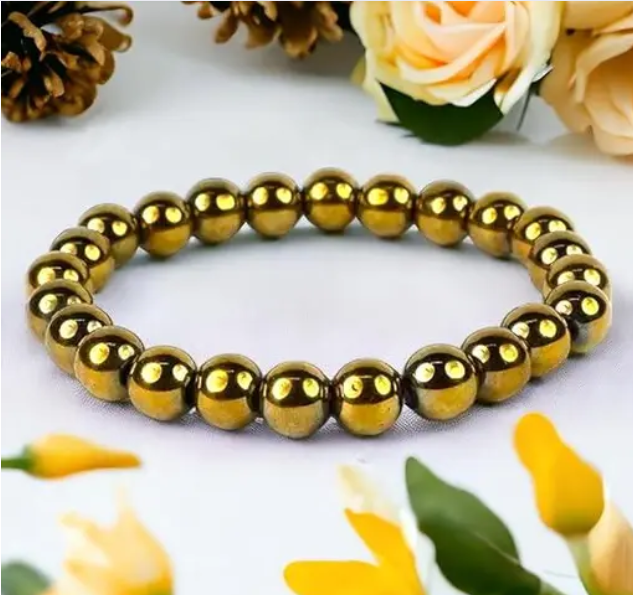Gold beaded bracelet on a white surface with flowers in the background